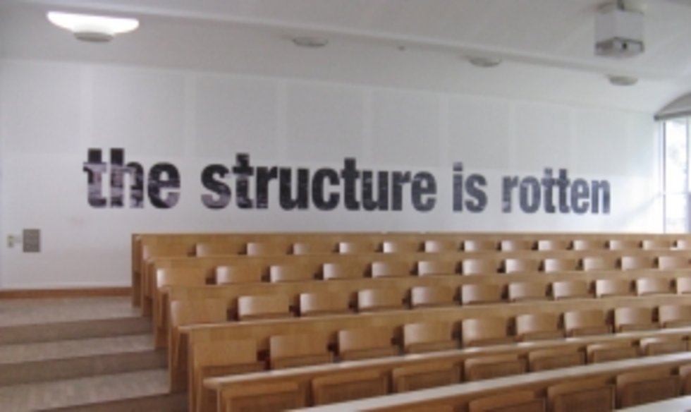 Foto der Arbeit "No Replastering, the Structure is Rotten" (2013) von Oliver Ressler im Hörsaal 1 der KU Linz.