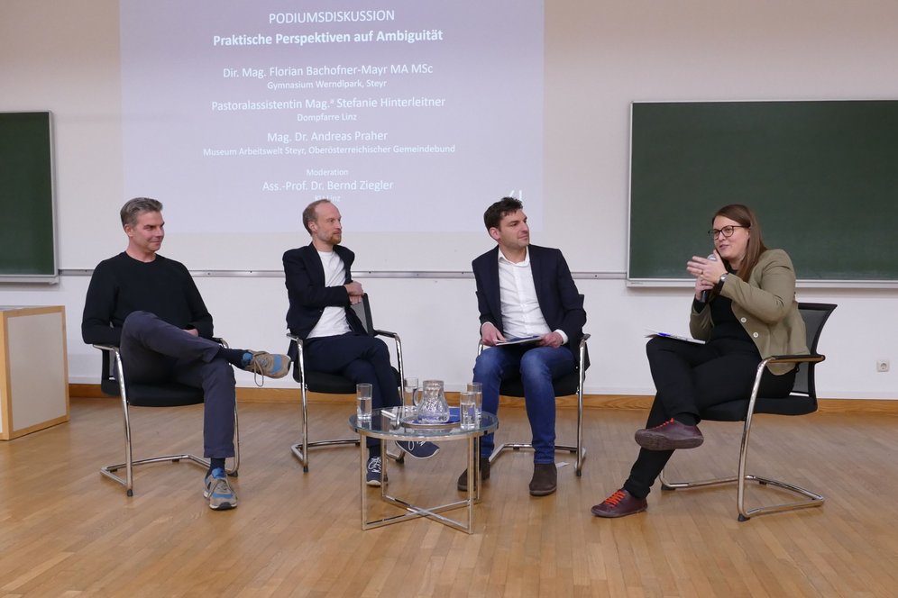 Podium mit drei Diskutant:innen plus Moderator.