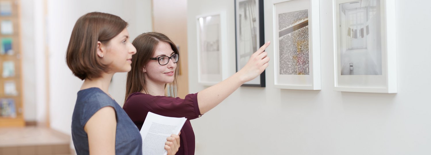 Kunstwissenschaft studieren an der Katholischen Privat-Universität Linz. Zwei weibliche Studierende betrachten Gemälde an der Wand.