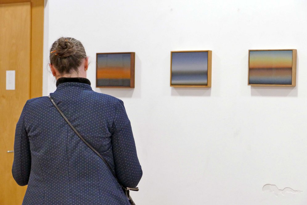 Frau betrachtet Gemäldeserie "Light Phenomena" von Mathias Kessler.