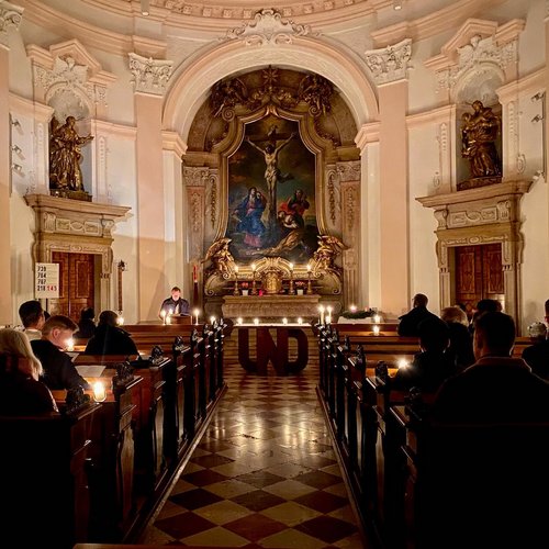 Picture of the KU chapel during liturgy, with people having candles, and the word "und" in front of the altar 