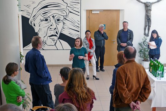 Kunstgespräch zur Mittagszeit mit Gastkuratorin Sarah Jonas, dem Illustrator Thomas Fatzinek und Prof.in Monika Leisch-Kiesl im Foyer der KU Linz vor einem Wandbild des Künstlers.