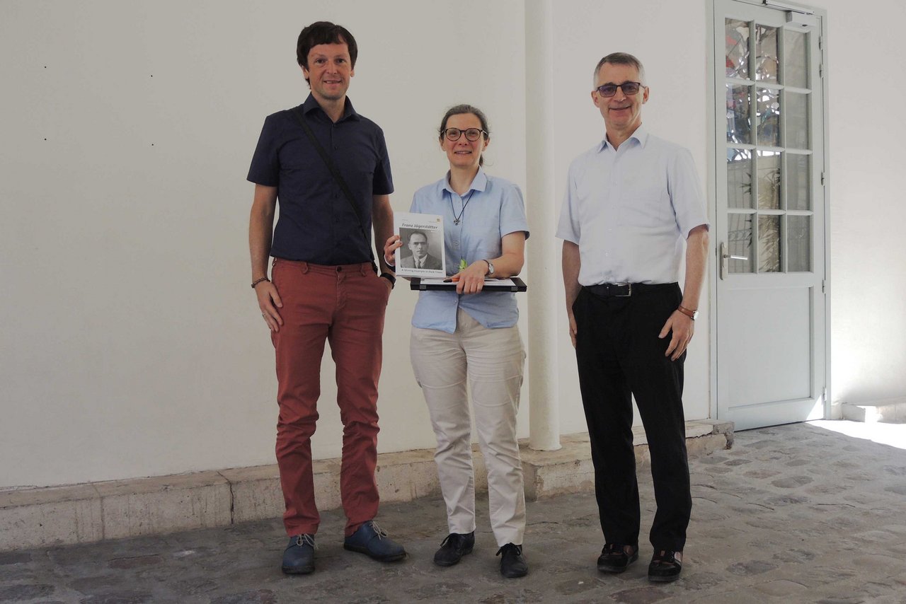 Picture of Andreas Schmoller and two colleagues, holding a book about Franz Jägerstätter