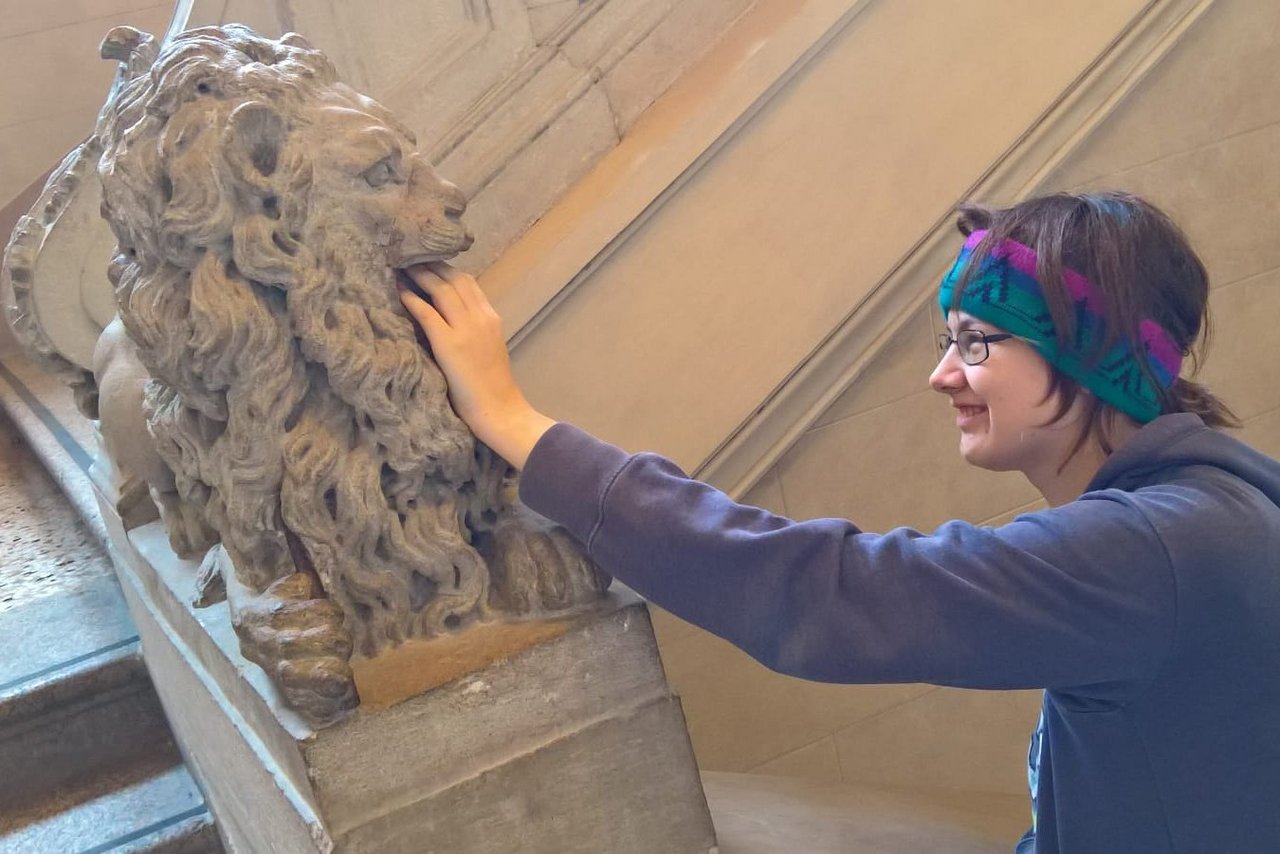 A student putting her hand into a lion statue's mouth