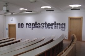 Foto der Arbeit "No Replastering, the Structure is Rotten" (2013) von Oliver Ressler im Hörsaal 1 der KU Linz.