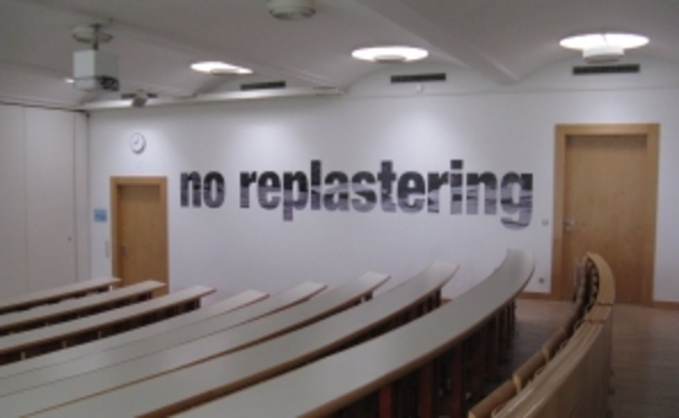 Foto der Arbeit "No Replastering, the Structure is Rotten" (2013) von Oliver Ressler im Hörsaal 1 der KU Linz.