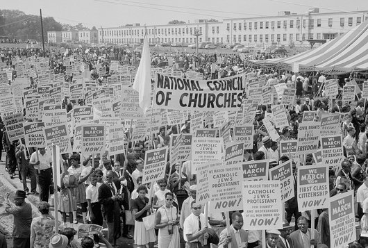 Historische Schwarz-Weiß-Fotografie zeigt viele Menschen mit Plakaten "We march for".